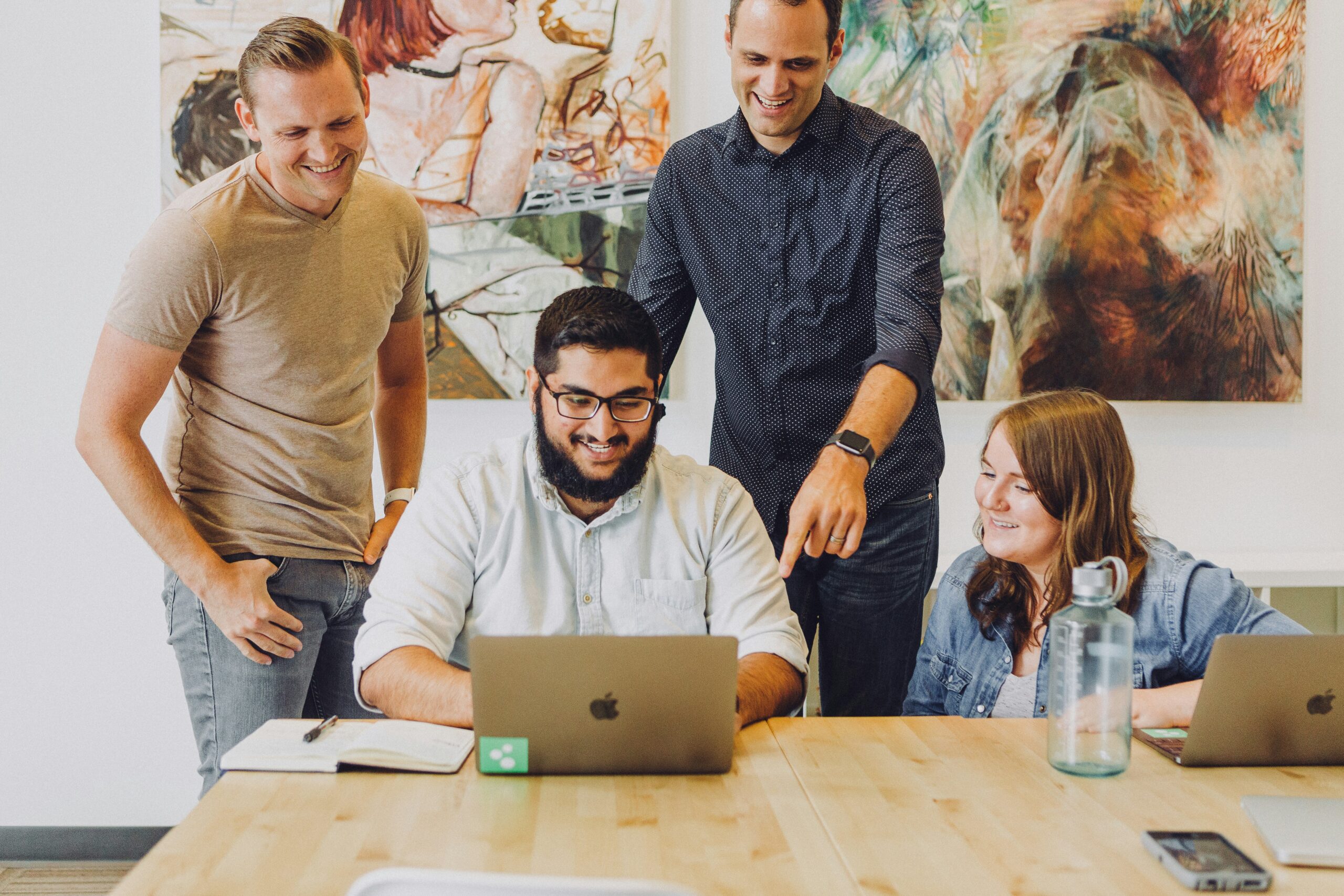 Four colleagues gathered around a laptop, smiling and collaborating